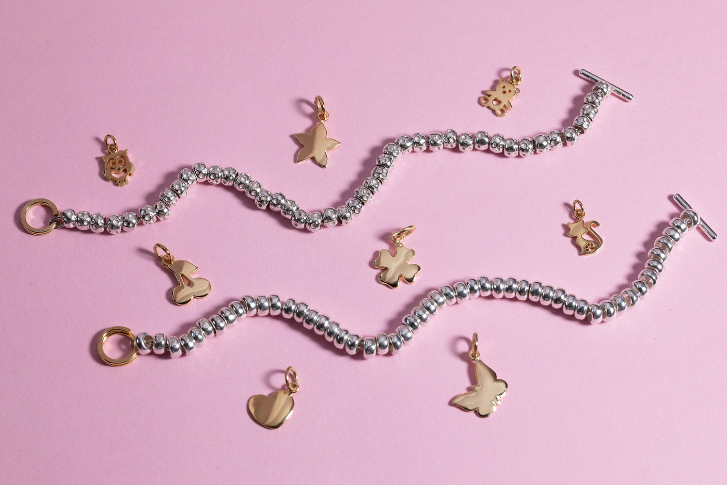 Bracciali in argento con charms dorati a forma di cuore, stella, quadrifoglio e farfalla su sfondo rosa – gioielli artigianali ViMon Gioielli.