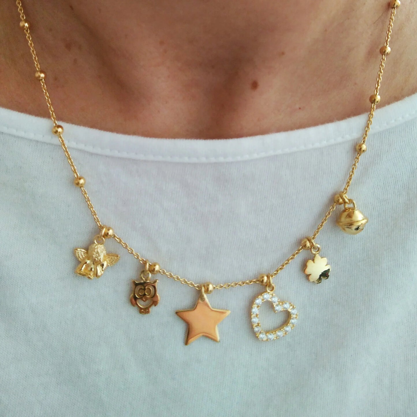 ragazza donna indossa la collana in argento 925 con placcatura oro giallo 18 kt con vari ciondoli pendenti charms angelo puttino gifo stellina cuore quadrifoglio campanellino consiglio regalo per natale 2020 compleanno serata di festa