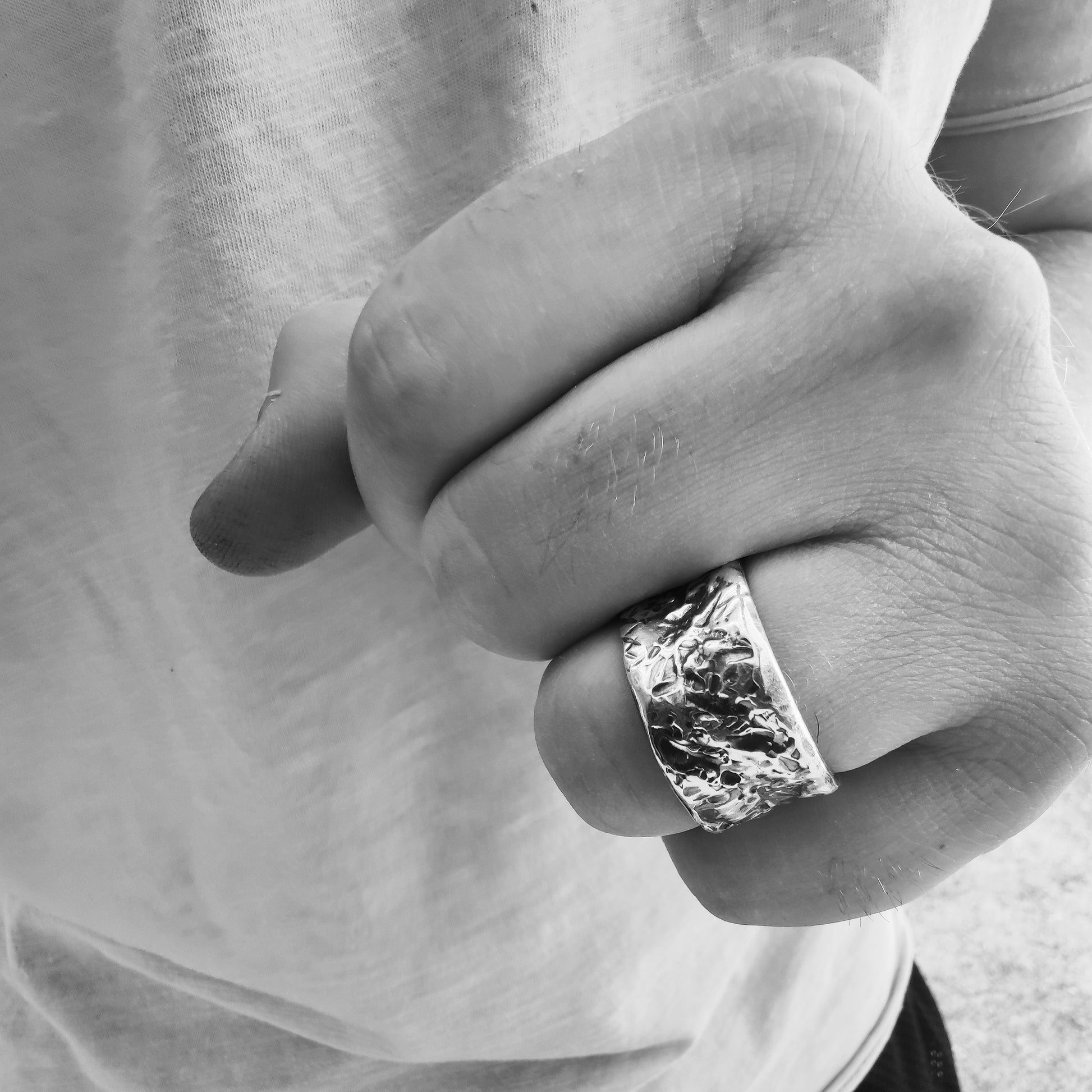 Mano maschile con anello in argento 925 martellato artigianale, design largo e texture irregolare, indossato su dito anulare.