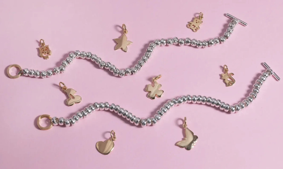 Bracciali in argento con granelli e charm dorati a forma di cuore, stella, farfalla e gatto su sfondo rosa