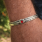 Bracciale rigido da uomo in argento 925 con incisioni geometriche e pietra corindone rosso taglio quadrato, indossato al polso 