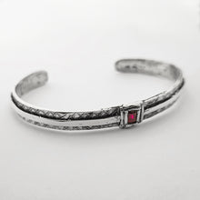 Carica l&#39;immagine nel visualizzatore di Gallery, Bracciale rigido da uomo in argento 925 artigianale con incisioni geometriche e pietra rossa quadrata centrale, fotografato in primo piano su fondo bianco minimal.
