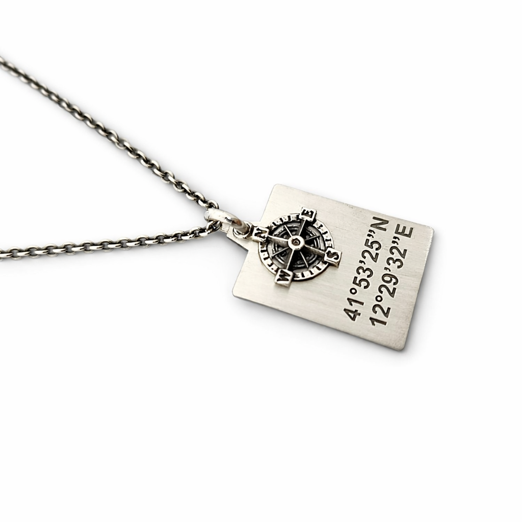 Dettaglio collana in argento 925 con piastrina incisa coordinate GPS e bussola, catena visibile, sfondo bianco