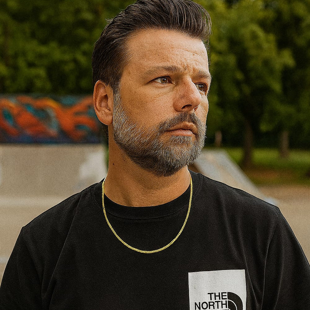 Collana uomo oro giallo indossata in look urban street style, abbinata a t-shirt nera brandizzata e sfondo skate park